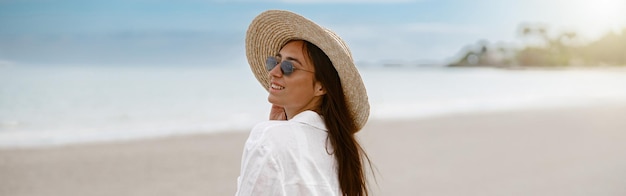 Viaggiatore di bella donna in un cappello in piedi sulla spiaggia tropicale e distogliendo lo sguardo concetto di vacanza