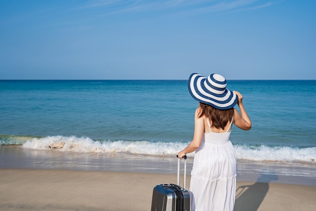 Viaggiatore di giovane donna asiatica con bagagli in spiaggia di sabbia tropicale