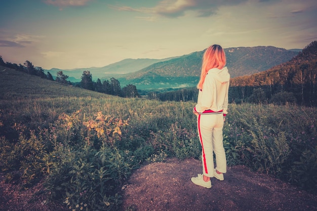 Viaggiatore di giovane donna in piedi sulla grande scogliera in montagna e guarda in lontananza al tramonto Concetto di libertà Effetto vintage filtrato giovane ragazza bionda guarda in lontananza la bellissima natura