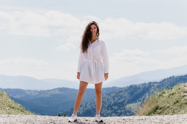 Viaggiatore di ragazza sorridente in montagna. Donna attraente che posa sulle colline verdi Turismo