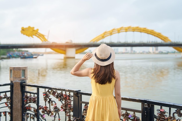 Viaggiatore donna con abito giallo in visita a Da Nang Visita turistica della vista sul fiume con il ponte del drago al ponte della serratura dell'amore Punto di riferimento e popolare concetto di viaggio in Vietnam e nel sud-est asiatico