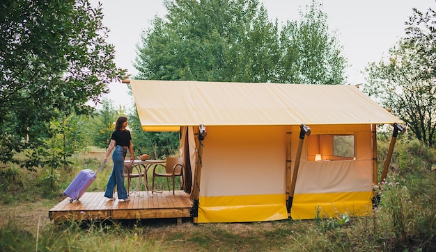 Viaggiatore donna con bagagli che si spostano verso la camera da letto di un'accogliente casa glamping Tenda da campeggio di lusso per vacanze estive all'aperto e vacanze Concetto di stile di vita