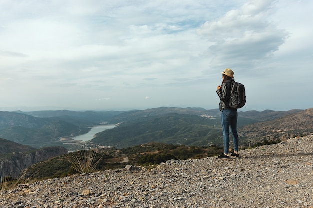 Viaggiatore donna con cappello in piedi su uno sfondo di montagne verdi