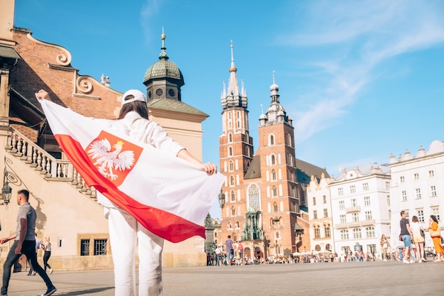 Viaggiatore donna ricoperta di bandiera polacca al centro della città di Cracovia