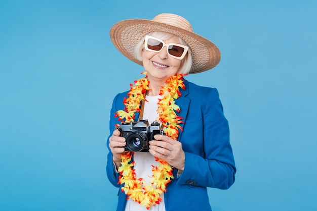 Viaggiatore donna senior con fotocamera retrò isolata su sfondo blu