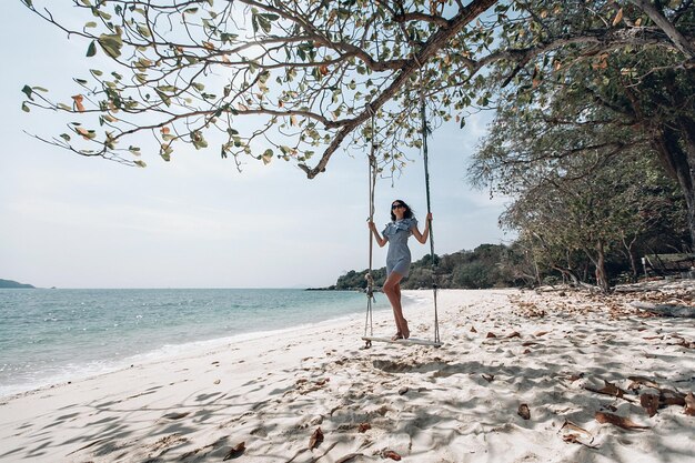 Viaggiatore felice donna in abito stile pin-up plaid bianco e nero rilassante sull'altalena. Spiaggia turistica del mare Tailandia, Asia, viaggio di viaggio di vacanza di vacanza estiva. Phuket. Tailandia