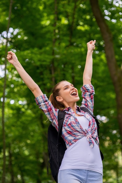 Viaggiatore felice. Inquadratura dal basso di una giovane donna felice con lo zaino che tiene le braccia alzate ed esprime positività stando in piedi nella natura