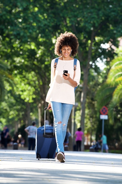 Viaggiatore felice integrale che cammina con la valigia e cellulare nel parco