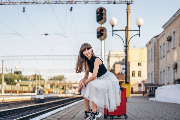 Viaggiatore femminile con il treno in attesa della valigia rossa sulla stazione ferroviaria