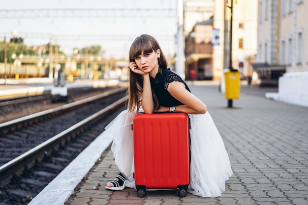 Viaggiatore femminile con il treno in attesa della valigia rossa sulla stazione ferroviaria