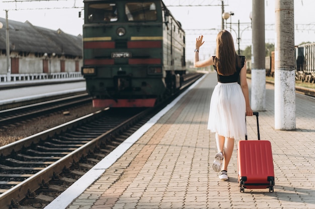 Viaggiatore femminile del brunette con la valigia rossa che cammina sulla stazione raiway