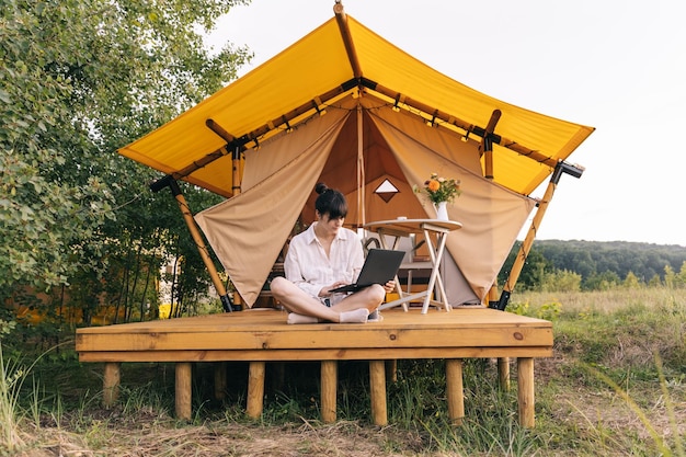 Viaggiatore femminile seduto accanto alla tenda da campeggio e utilizzando il computer portatile notebook funzionante