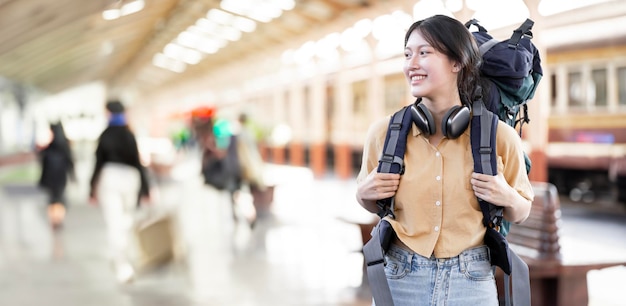 Viaggiatore giovane donna con zaino in attesa del treno Zaino in spalla asiatico sulla piattaforma ferroviaria alla stazione ferroviaria Viaggio di vacanza e concetto di viaggio estivo