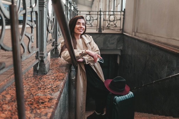 Viaggiatore grazioso della ragazza in un cappotto che sta sulle scale della stazione ferroviaria