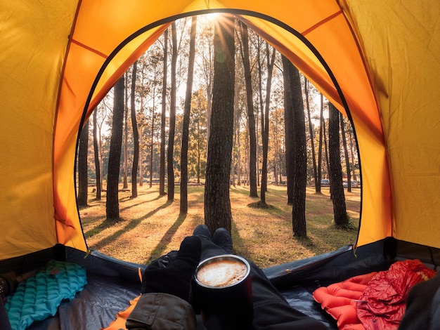 Viaggiatore in possesso di caffè rilassante all'interno di una tenda arancione e godersi la vista del tramonto sulla pineta nel parco nazionale