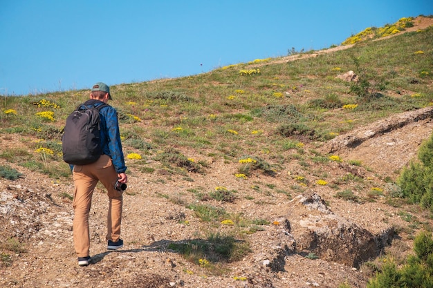 Viaggiatore maschio escursionista con zaino smartphone e fotocamera in mano va in salita Viaggi e stile di vita sano