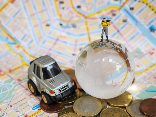 Viaggiatore o viaggiatore zaino in spalla in miniatura su globo di vetro, monete in euro e mappa.
