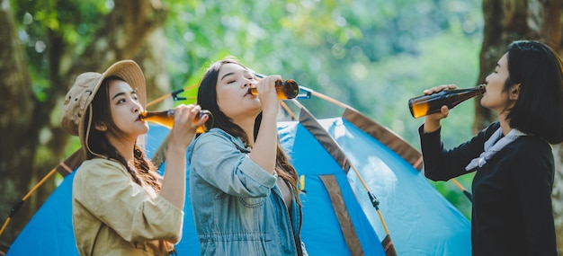 Viaggiatori di giovani donne e ragazze che si rilassano sulle sedie da campo in tenda Stanno applaudendo e bevendo birra durante il campeggio parlando con divertimento e felici insieme