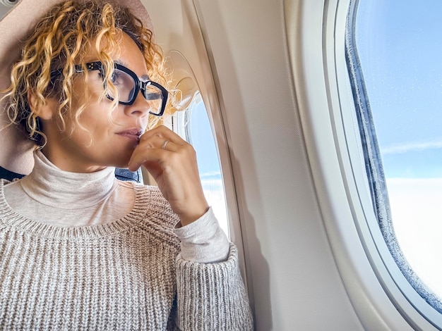 Viaggiatrice attraente che indossa occhiali che guarda fuori dalla finestra seduta all'interno del volo dell'aereo Concepto di persone e trasporto aereo Destinazione di vacanza Destinazione vacanza Donna adulta in viaggio