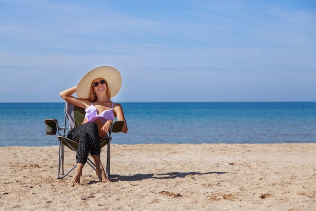 viaggio al mare. ragazza in costume da bagno e cappello a prendere il sole sulla spiaggia. turista seduto sulla sabbia. abbigliamento per il tempo libero. copia spazio