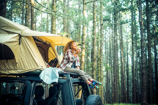 Viaggio avventuroso e viaggio stile di vita persone che utilizzano il veicolo come hoem con tenda sul tetto dell'auto Una donna turistica di stile di vita alternativo seduta fuori con boschi verdi e alberi ad alto fusto sullo sfondo