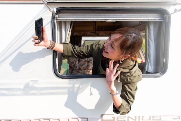 Viaggio di famiglia in auto Caravan su una bellissima vacanza. Giovane donna asiatica selfie con smartphone in roulotte con tazza di caffè bianco al mattino in