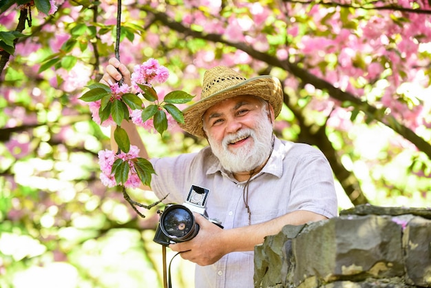 Viaggio di pensionamento Godersi il tempo libero Viaggi e turismo Catturare la bellezza Nonno felice Vacanze primaverili Foto di viaggio Fotografo in giardino fiorito Senior man tenere fotocamera professionale