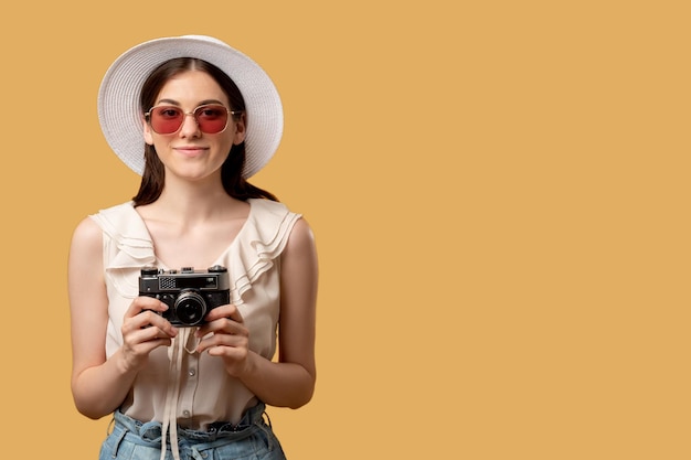 Viaggio di vacanza Cattura momenti Ricordi estivi Donna sorridente occhiali da sole cappello con fotocamera retrò pronta per scattare foto guardando dritto isolato su spazio copia beige Sfondo pubblicitario