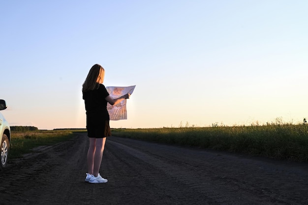 Viaggio in auto Una ragazza turistica in viaggio su strada con una mappa è in piedi vicino all'auto