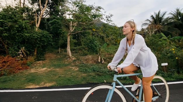 Viaggio in bicicletta La donna sulla bici blu in abiti bianchi sulla strada forestale La ragazza in bicicletta Ciclismo Cycle Fix Asia Thailandia giro turistico Scatta una foto con una bicicletta