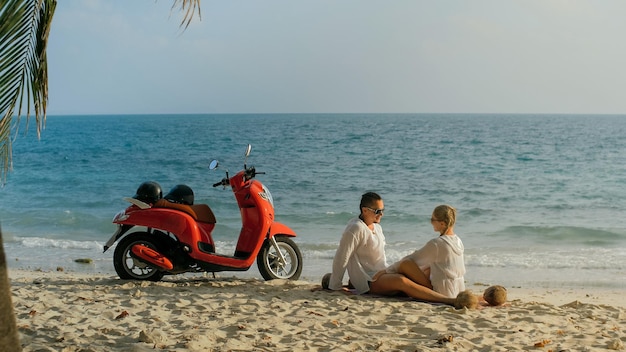 Viaggio in scooter Coppia adorabile su una moto rossa in abiti bianchi sulla spiaggia di sabbia