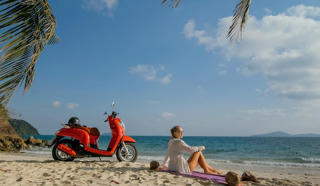 Viaggio in scooter Donna sola su una moto rossa in abiti bianchi sulla spiaggia di sabbia dall'oceano