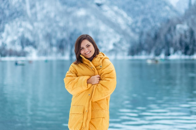 Viaggio invernale in tutta Europa. ritratto di una bella giovane donna in una giacca gialla sulla riva di un lago alpino in inverno. vista del lago alpino con neve.