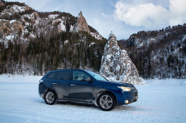 Viaggio invernale L'auto sullo sfondo di un paesaggio invernale con montagne innevate e rocce sullo sfondo