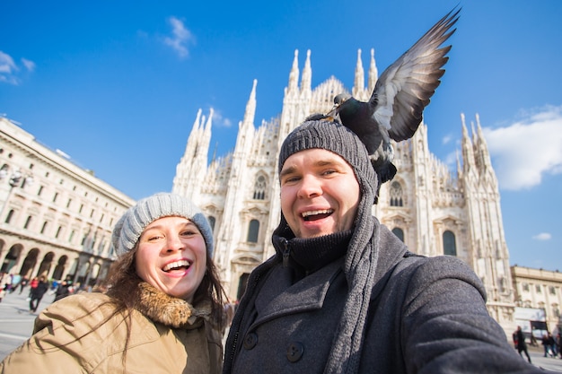 Viaggio, Italia e concetto di coppia divertente - Turisti felici che prendono un autoritratto con i piccioni davanti al Duomo di Milano