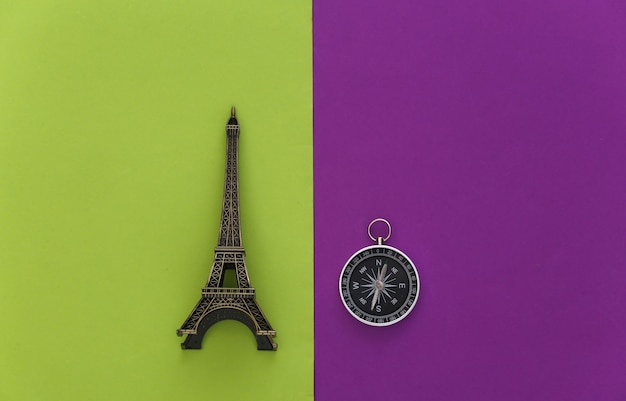 Viaggio minimalista, avventura piatta. Bussola e figurina della torre eiffel su sfondo verde viola. Vista dall'alto