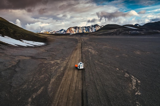 Viaggio su strada con auto turistica 4x4 parcheggiata nel deserto vulcanico con cratere su strada sterrata a Landmannalaugar nelle Highlands islandesi