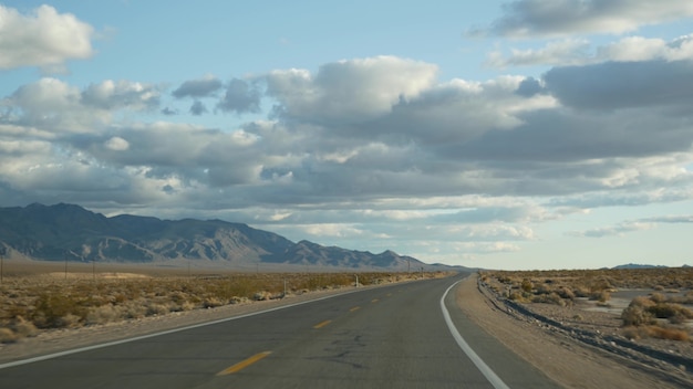 Viaggio su strada, guidando un'auto dalla Death Valley a Las Vegas, Nevada, USA. Autostop in viaggio in America. Viaggio in autostrada, atmosfera drammatica, nuvole, montagne e deserto del Mojave. Vista dall'auto