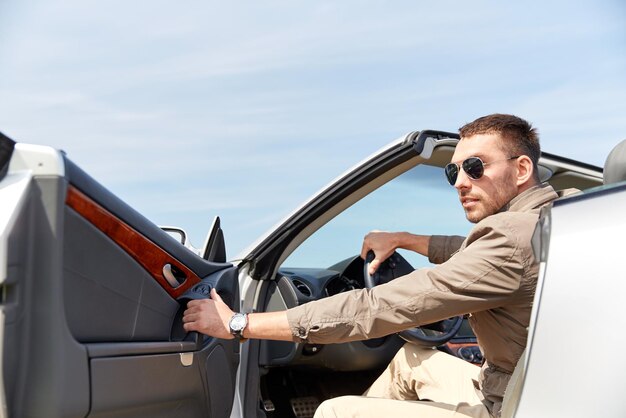 viaggio su strada, viaggio, trasporto, tempo libero e concetto di persone - uomo felice che apre la porta dell'auto cabriolet all'aperto