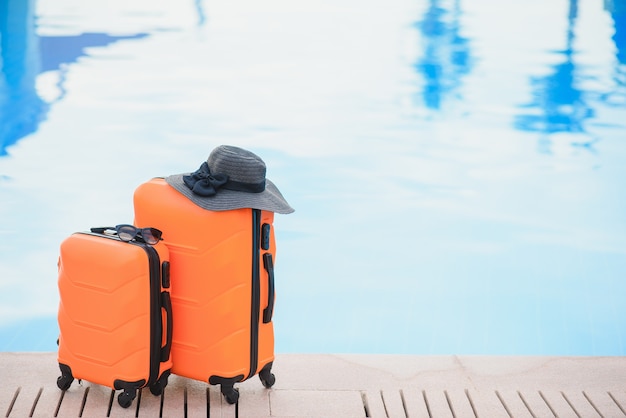 viaggio, vacanze estive e concetto di vacanza. valigia rosa con cappello sullo sfondo della piscina dell'hotel.