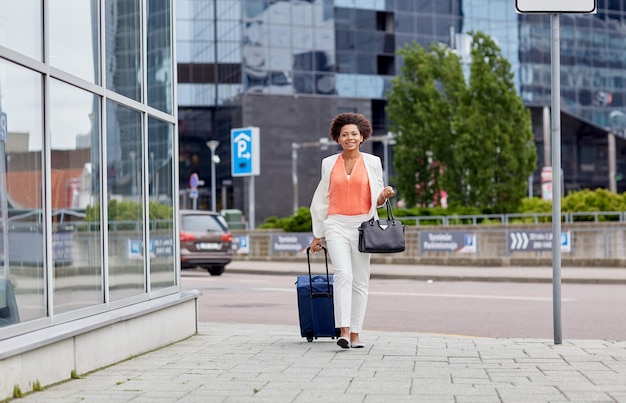 viaggio, viaggio d'affari, concetto di persone e turismo - felice giovane donna afroamericana con borsa da viaggio che cammina per la strada della città