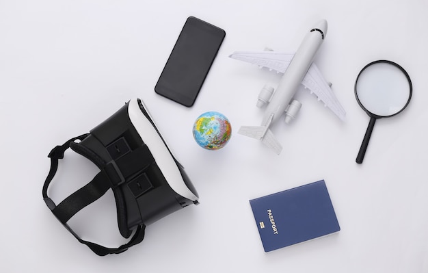 Viaggio virtuale. Cuffie per realtà virtuale con globo, passaporto, smartphone e aereo su sfondo bianco. Vista dall'alto