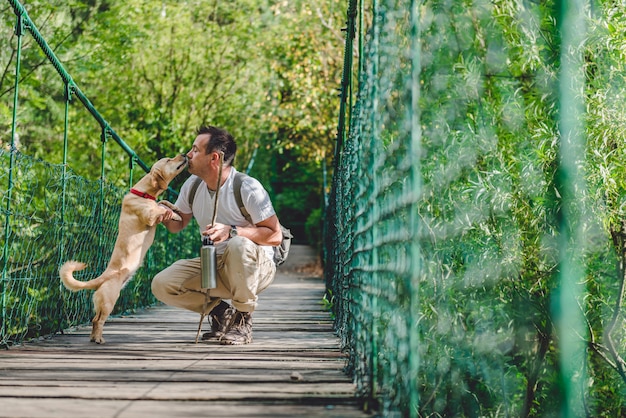 Viandante con il cane che riposa sul ponte sospeso di legno