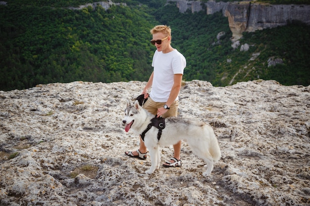 Viandante con il cane del husky siberiano che esamina bella vista in montagne