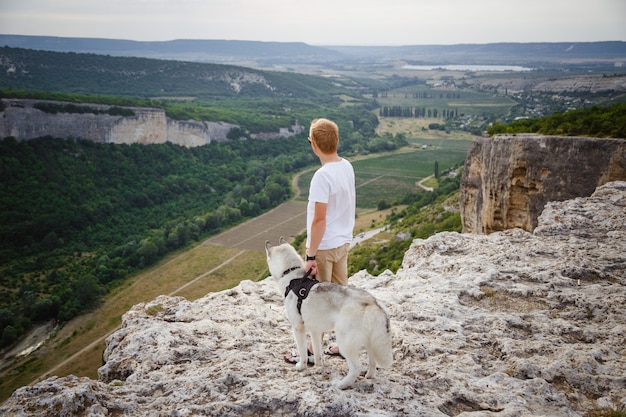 Viandante con il cane del husky siberiano che esamina bella vista in montagne