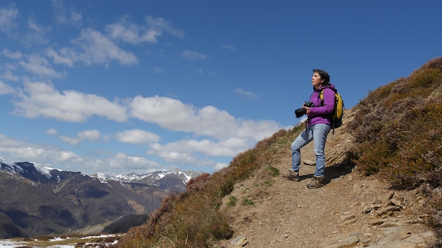 Viandante con la macchina fotografica e lo zaino che prendono immagine di bella montagna