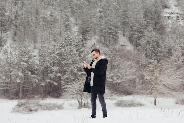 Viandante del giovane sta utilizzando smartphone sulla montagna innevata.