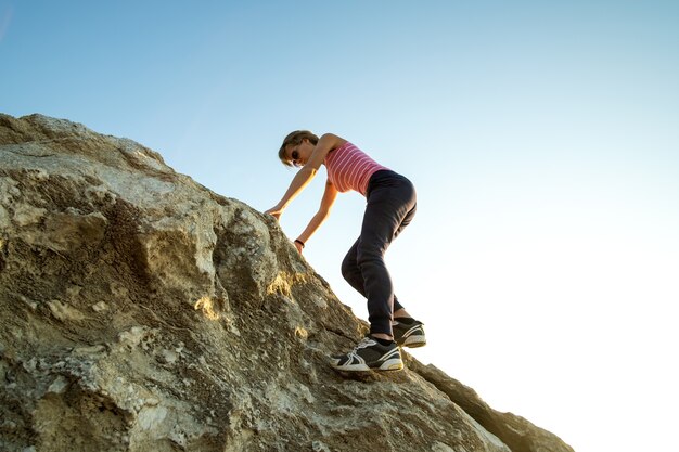 Viandante della donna che scala grande roccia ripida un giorno soleggiato. La giovane scalatrice supera la difficile via di arrampicata. Ricreazione attiva nel concetto di natura.