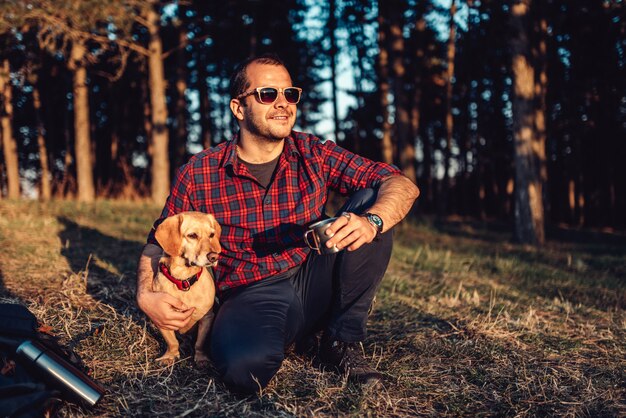 Viandante felice con il cane che riposa sull'erba e che beve caffè