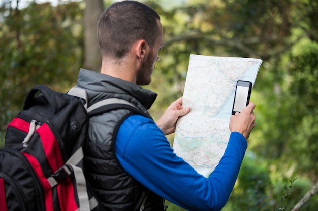 Viandante maschio che esamina mappa e telefono cellulare